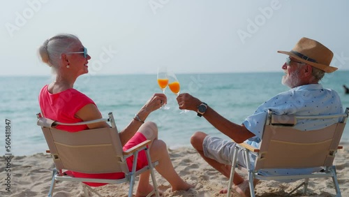 Happy Senior couple drinking orange juice together at tropical beach. Elderly retired husband and wife enjoy summer outdoor lifestyle on beach at holiday. travel and vacation after retirement concept.