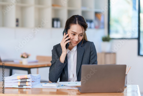 Beautiful Asian businesswoman sitting smiling and talking on the phone in the office with customers with documents in a friendly and casual manner.