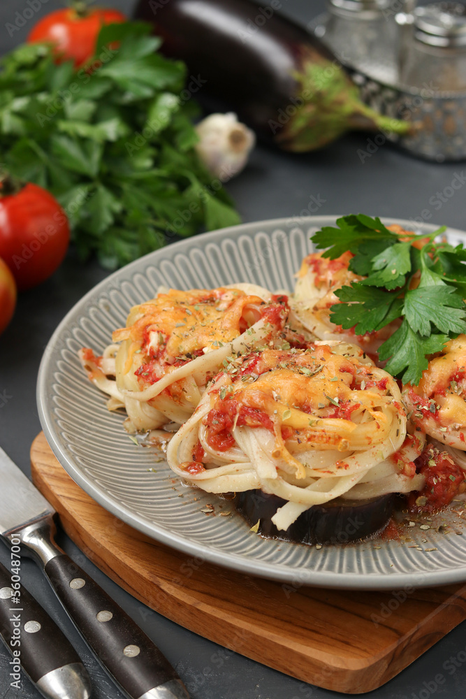 Fototapeta premium Spaghetti with eggplants, tomatoes and cheese on a gray plate on wooden board. Vegetarian food