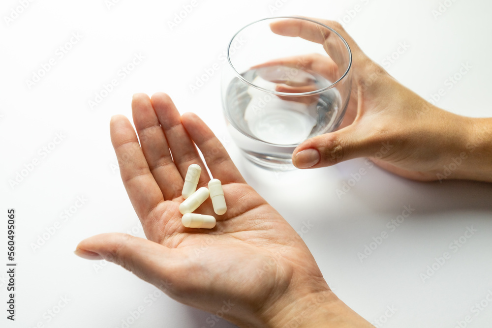 Hands holding pills and a glass of water, supplementation and health, vitamin replenishment concept