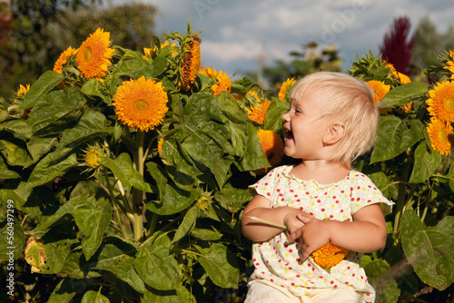 little blonde girl laughs against the background of sunflowers