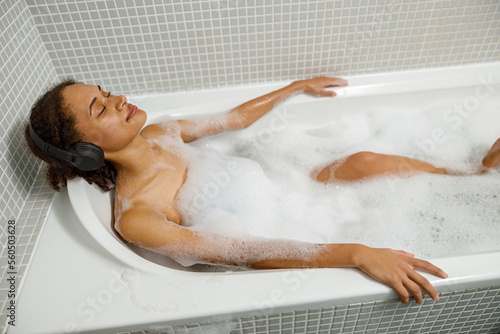 Photography Afro American woman takes bubble bath in bathtub and listen music