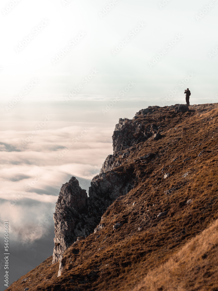 person standing on a rock cliff  with a sea of clouds below