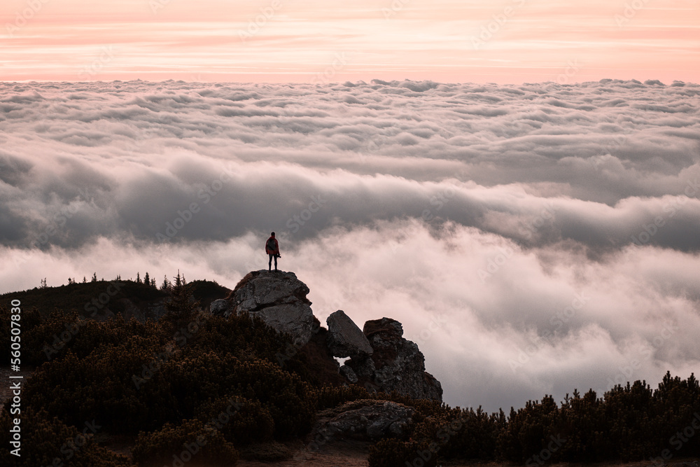 Traveler standing on cliff edge mountain top above sunset clouds travel adventure lifestyle summer journey vacations