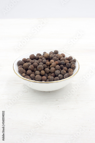 Allspice peas scattered in a white bowl on white wooden background