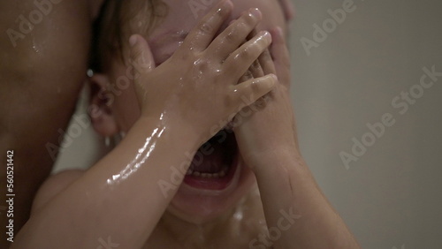 Upset baby washing hair. Crying toddler rubbing eyes and face