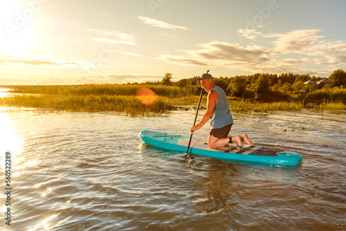 a man in shorts sits on a sup board at sunset in the water. © finist_4