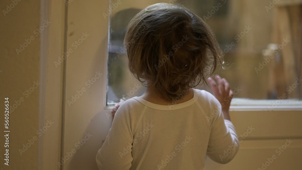 Toddler child staring outside standing by window at home Toddler child staring outside standing by window at home