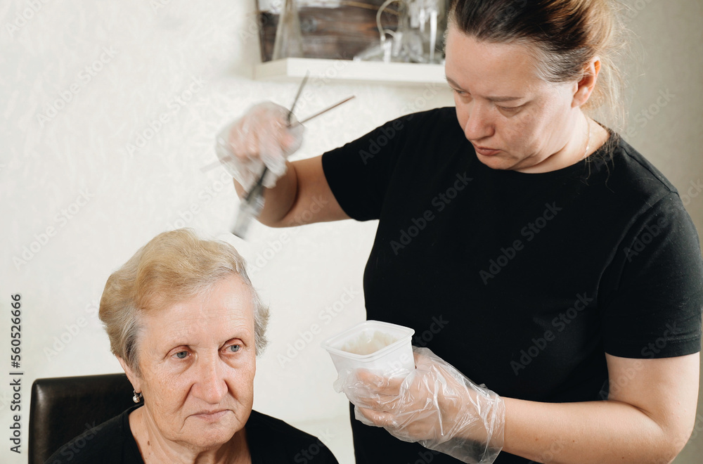 A woman daughter paints her elderly mother's hair with a brush. A woman daughter paints her elderly mother's hair with a brush.