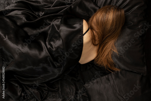 Woman sleeps in a bed on black bed sheet. Sleeping concept.