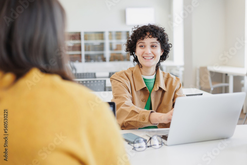 two women in library or coworking are sitting opposite each other working on laptop. meeting and negotiations of two colleagues, classmates. scientific work in office or university. success, career photo