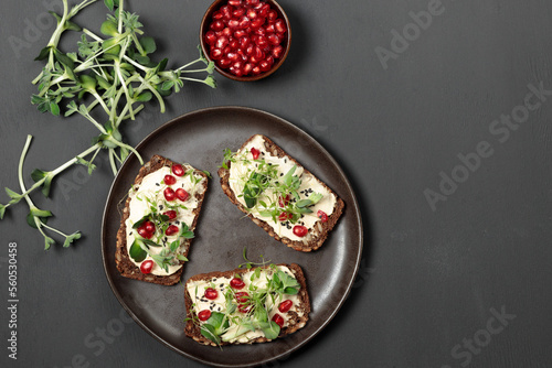 Sandwiches with soft cheese, microgreens, pomegranate seeds. Close-up on a black background, a glass of juice in the background.