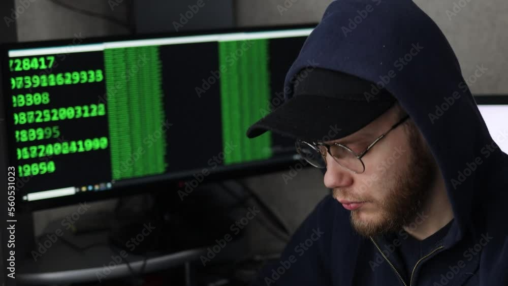 male hacker in glasses and a cap at a computer with green code numbers. male hacker in glasses and a cap at a computer with green code numbers.