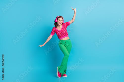 Full length photo of carefree lovely girl with curly hairdo dressed pink top dancing look empty space isolated on blue color background