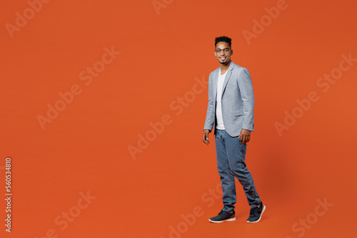 Full body side view happy young employee business man corporate lawyer wear classic formal grey suit shirt glasses work in office look camera go posing isolated on plain red orange background studio.