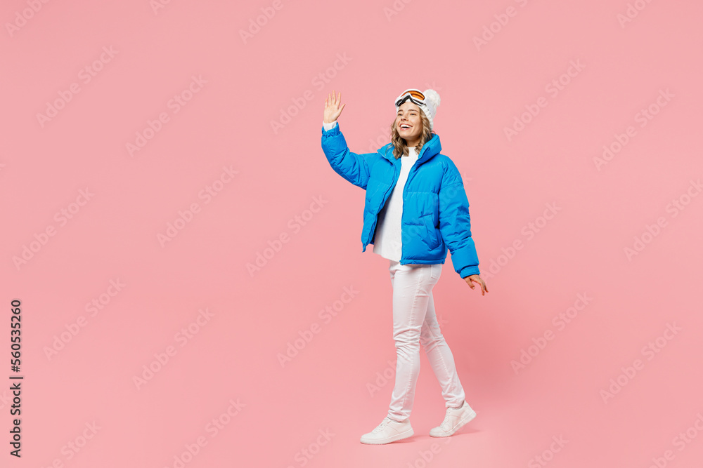 SIde view fun snowboarder woman wear blue suit goggles mask hat ski padded jacket walking go waving hand isolated on plain pastel pink background Winter extreme sport hobby weekend trip relax concept SIde view fun snowboarder woman wear blue suit goggles mask hat ski padded jacket walking go waving hand isolated on plain pastel pink background Winter extreme sport hobby weekend trip relax concept