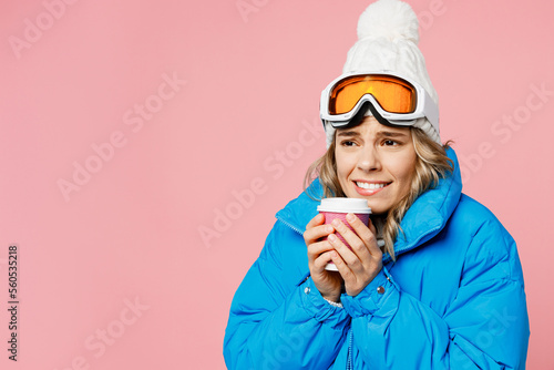 Snowboarder frozen woman wear blue suit goggles mask hat ski padded jacket hold paper cup coffee to go isolated on plain pastel pink background. Winter extreme sport hobby weekend trip relax concept.