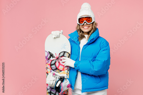 Snowboarder smiling woman wear blue suit goggles mask hat ski padded jacket hold snowboard behind neck isolated on plain pastel pink background. Winter extreme sport hobby weekend trip relax concept. #560535255