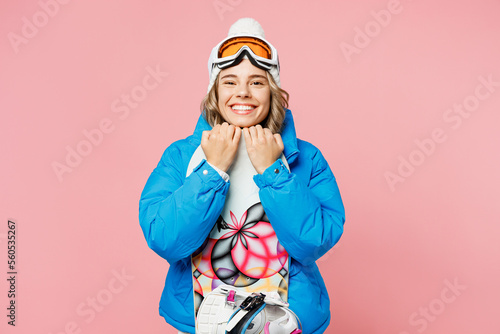 Snowboarder smiling woman wear blue suit goggles mask hat ski padded jacket hold snowboard look camera isolated on plain pastel pink background. Winter extreme sport hobby weekend trip relax concept.