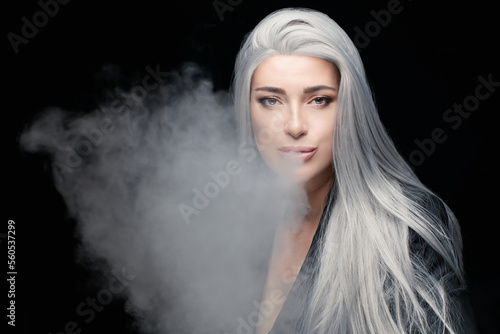 Fashion art portrait of silver haired model woman blowing a big smoke cloud. Smoking girl vaping an electronic cigarette. isolated on black background with copy space