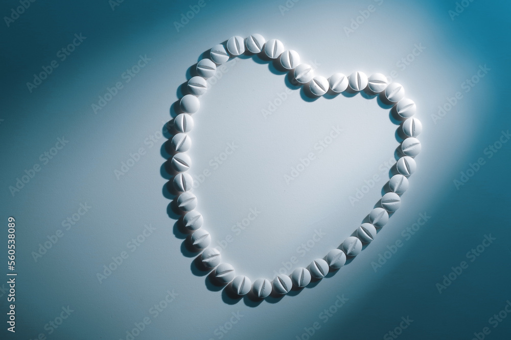 Obraz premium Heart shape of white pills on light white background in blue hard light with shadow, top view