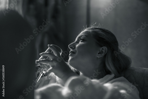 Young woman in a bathrobe, resting on a sofa, drinking white wine. © Michaela