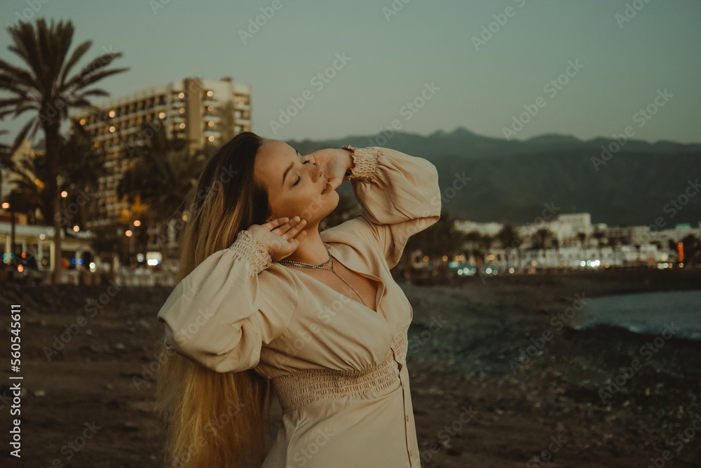 Girl on the beach with long hair, summer mood. Sunset, woman in a beautiful dress on vacation, and accessories, palm trees on mito with the sea in the background.
