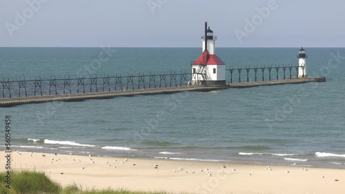Lighthouses at St. Joseph, MI. Closeup static shot from high on a sand dune shows the main lighthouse and outer beacon with seagulls on the beach in the foreground.