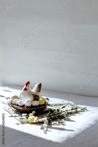 Ceramic chicken in a nest with colorful chocolate eggs on a light background