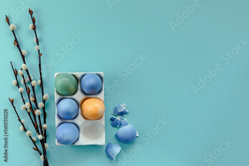 Colorful Easter eggs in a stand on a blue background next to willow branches