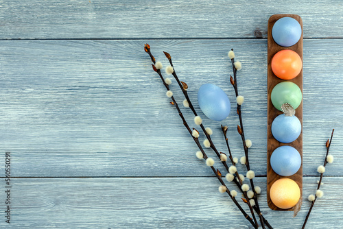 Colorful Easter eggs in a stand on a wooden blue table next to willow branches