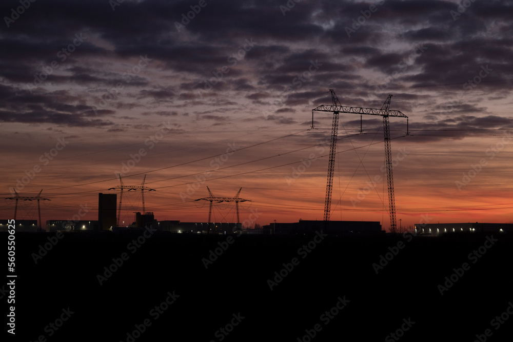 silhouettes of power lines in beautiful sunset colors.high voltage electric transmission tower.Industrial zone. there are factories in the background