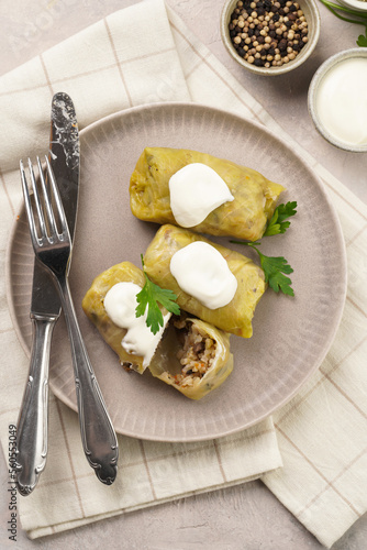 Three vegetarian cabbage rolls stuffed with rice, mushrooms, carrots and onions topped with vegan sour cream, traditional ukrainian dish during religious fasting time periods on a grey plate, top view