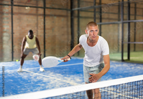 Padel player playing padel in a padel court indoor behind the net © JackF