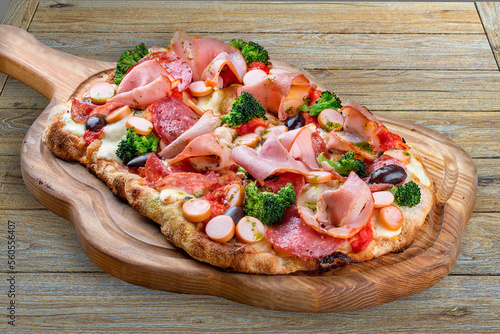 Pizza with salami, ham, vienna sausages, kalamata, olives, broccoli, pelati, pesto. Roman pizza rectangular on wood background