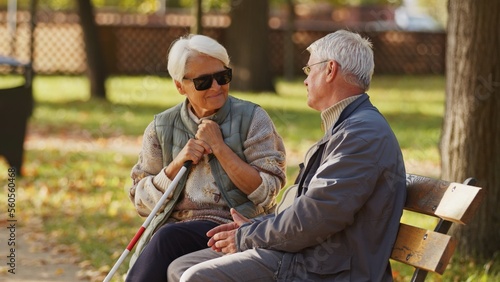 Blind senior woman with dark sunglasses on with her husband in the park. High quality photo
