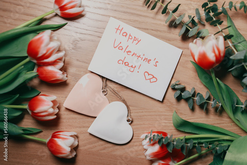 Bouquet of tulips on the table with a card and hearts. Valentines flat lay concept. Top view.