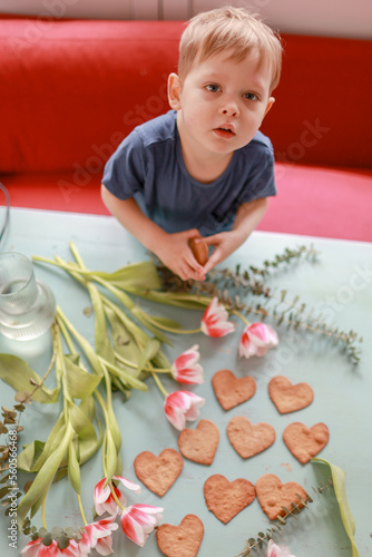 Baby boy holding heart shaped cookies on the table.Valentines, mothers, womens day, wedding or birthday flat lay concept. Top view.