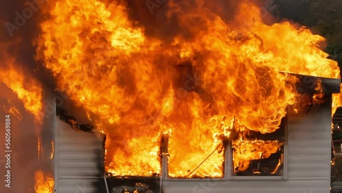 Hot flames rising as a small building is destroyed by a large fire. Slow motion, close up footage of a small house on fire.