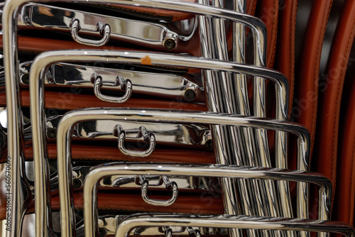 Selective focus at the metal armrest of the vertical stack modern brown chairs beside stack of  stack old wooden chairs.   © Peeradontax