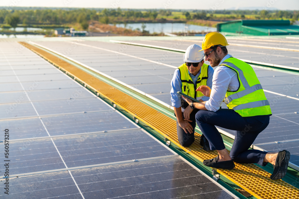 Professional man engineer using digital tablet maintaining solar cell panels together on building rooftop. Technician team working on ecological solar farm. Renewable clean energy industry concept. Professional man engineer using digital tablet maintaining solar cell panels together on building rooftop. Technician team working on ecological solar farm. Renewable clean energy industry concept.
