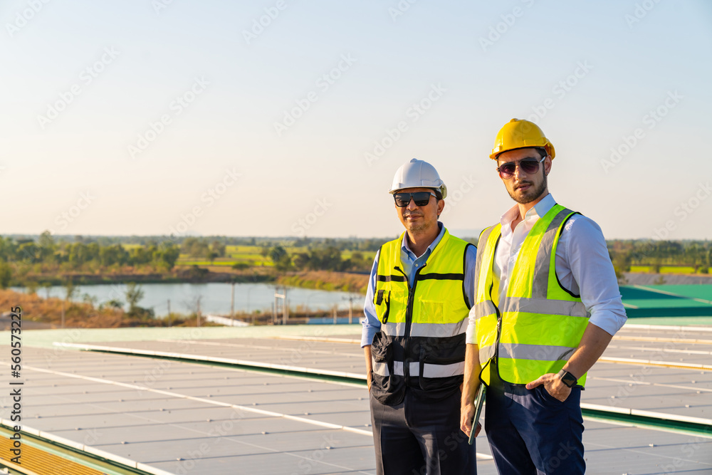 Portrait of Professional man engineer maintaining solar cell panels together on factory building rooftop. Technician team working on ecological solar farm. Renewable clean energy industry concept. Portrait of Professional man engineer maintaining solar cell panels together on factory building rooftop. Technician team working on ecological solar farm. Renewable clean energy industry concept.