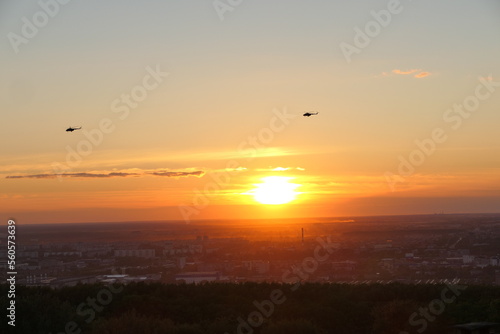 Two helicopters in the sky against the backdrop of the setting sun  Bright sunset.