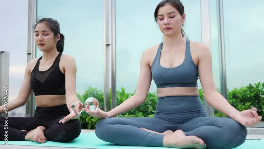 Asian woman and friend in sportswear and practicing lotus pose on yoga mat outdoors, woman doing yoga exercise Asian woman and friend in sportswear and practicing lotus pose on yoga mat outdoors, woman doing yoga exercise