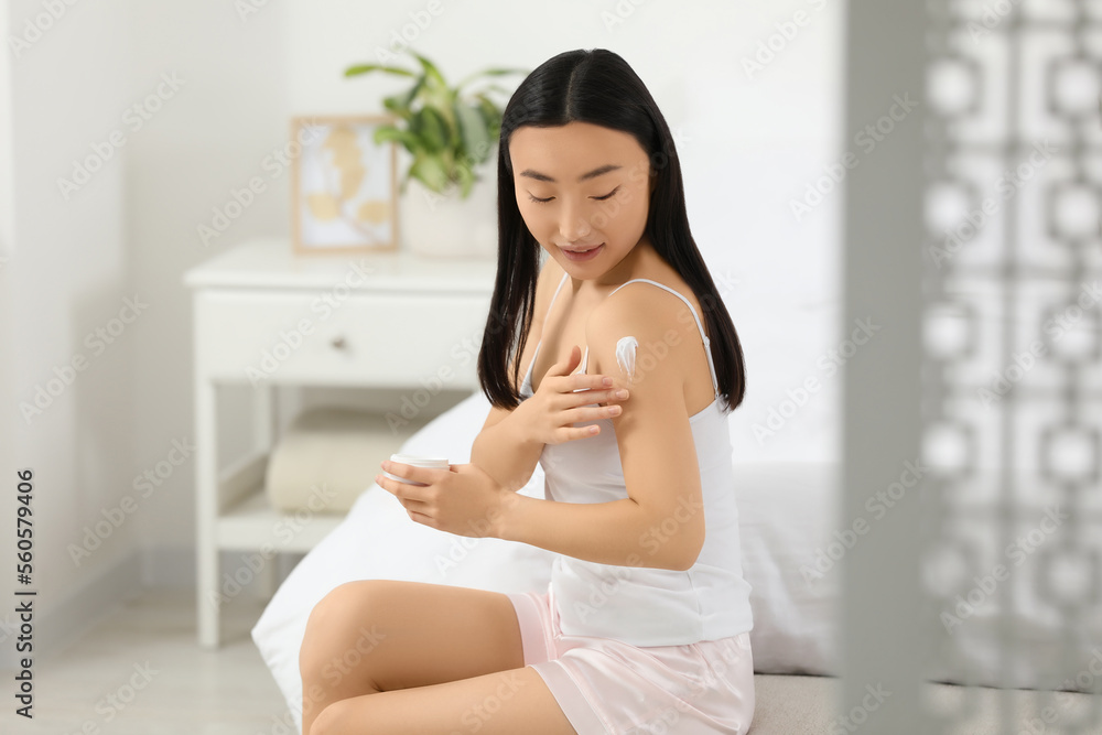 Beautiful young Asian woman applying body cream on shoulder in bedroom Beautiful young Asian woman applying body cream on shoulder in bedroom