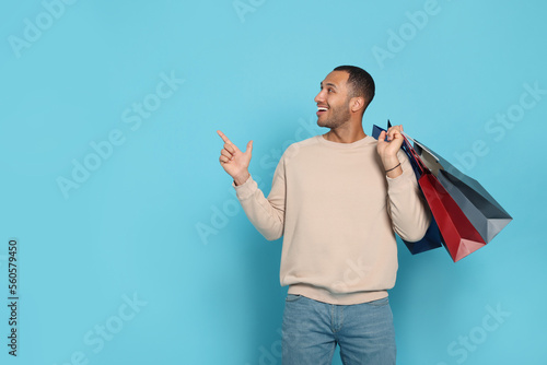 Happy African American man with shopping bags on light blue background. Space for text photo