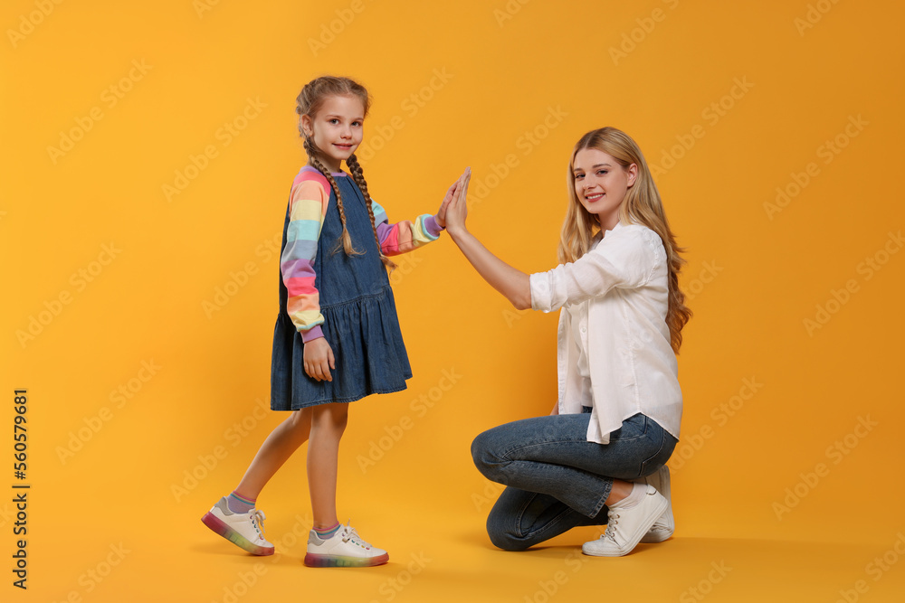 Naklejka premium Mother and daughter giving high five on orange background