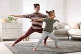 Young mother and her daughter practicing yoga together at home
