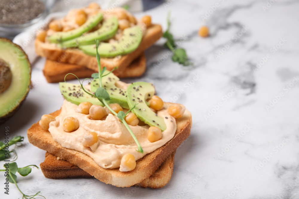Delicious sandwiches with hummus, avocado and chickpeas on white marble table. Space for text