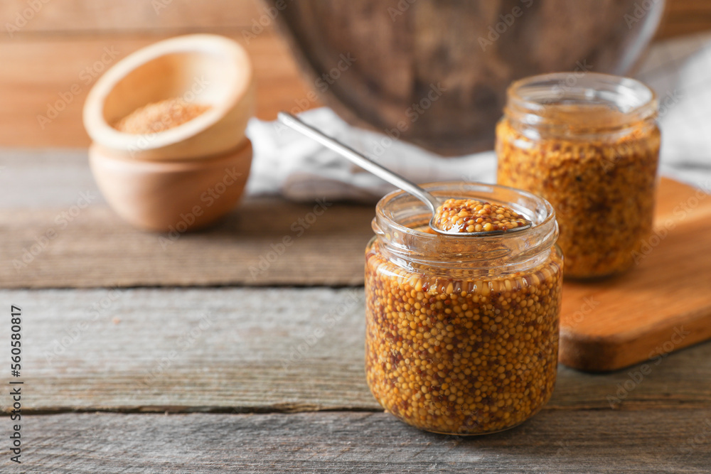 Jars and spoon of whole grain mustard on wooden table. Space for text Jars and spoon of whole grain mustard on wooden table. Space for text